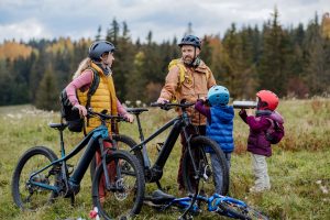 Young family with little children preparing for bicycle ride in nature, putting off bicycles from